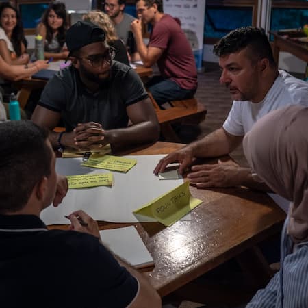 A diverse group of people engaged in a brainstorming session around a wooden table, discussing innovative solutions for water-related challenges. A diverse group of people engaged in a brainstorming session around a wooden table, discussing innovative solutions for water-related challenges.